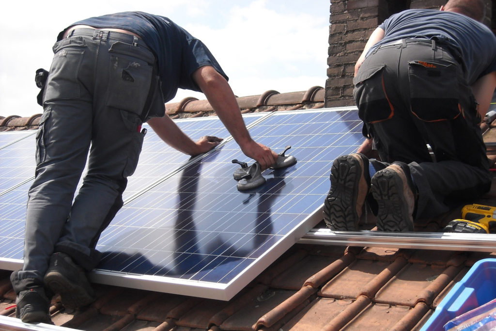 Two men fitting solar panels to a roof
