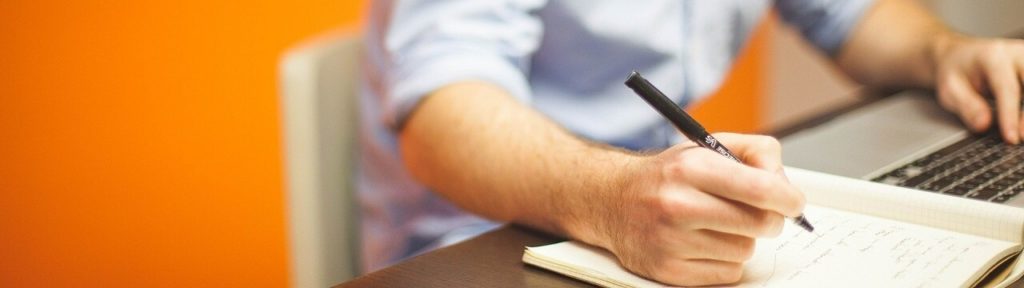 Man at desk using laptop with book and pen