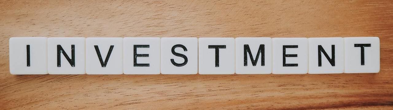 The word 'Investment' in Scrabble letters on a desk