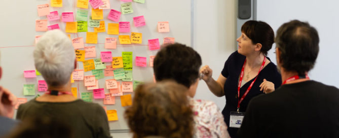 A trainer at a CAfS carbon literacy course with attendees looking at a whiteboard full of sticky notes