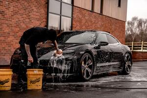 A man washing a car with buckets and a sponge