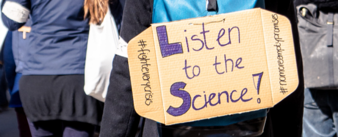 A protest sign displayed by a marcher saying: Listen to the science