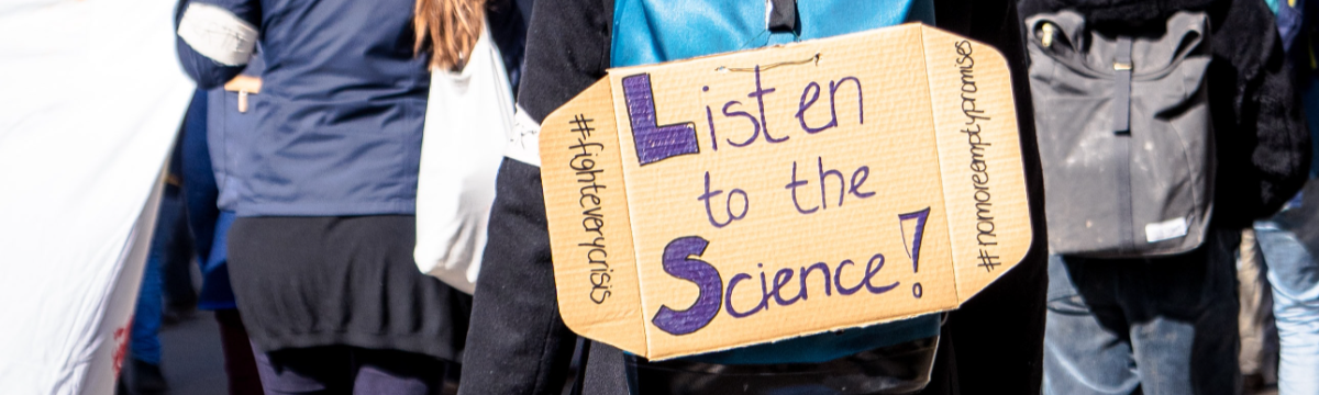 A protest sign displayed by a marcher saying: Listen to the science